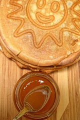 Pancakes and jar of honey with a spoon on a wooden board