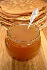 Pancakes and jar of honey with a spoon inside on a wooden board