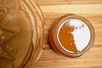 Pancakes and jar of honey on wooden board