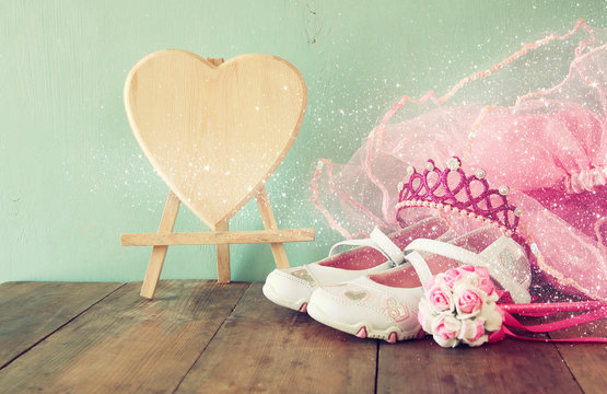 Small girls party outfit: white shoes, crown and wand flowers on wooden table. bridesmaid or fairy costume. vintage filtered
