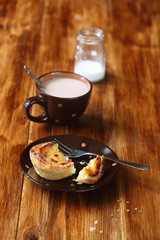 Broken  Portuguese Custard Tart (Pastel de Nata), cup of latte and little bottle of milk, on a wooden table.