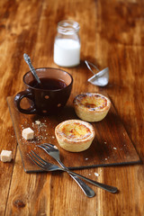 Traditional Portuguese Custard Tarts (Pastéis de Nata), cup of tea and little bottle of milk, on wooden board and table. 