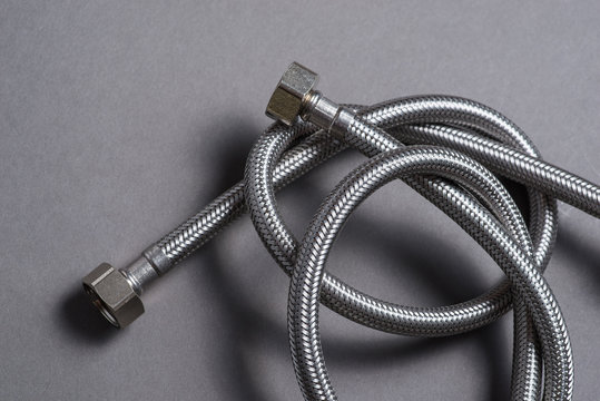 Braided stainless steel water hose over grey background