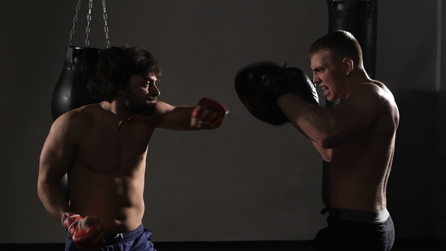 Artful young kickboxer fulfills blows with coach. 