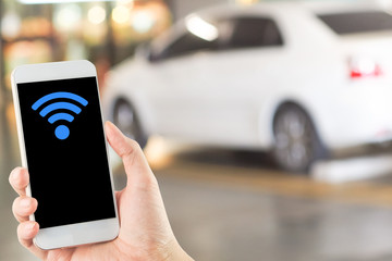 smartphone in hand with wi-fi icon on blurred car parking area