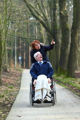 senior/ old man in wheelchair taken along by a care taker for a stroll through the woods early spring