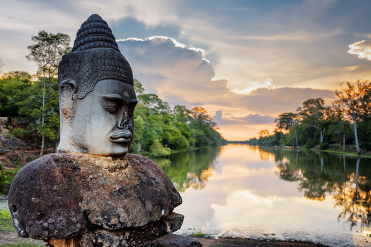 Stone Asura and sunset over moat surrounding Angkor, Cambodia