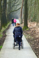 Fototapeta premium wheelchair/ care taker running through the woods with an old person in a wheelchair just to have some fun
