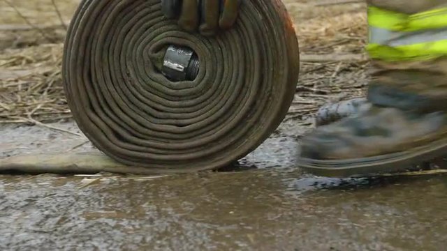 Trudging through mud and rain, the hands of a fireman roll up a water hose