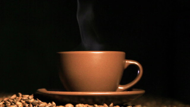 Cup of hot coffee, grains with steam   in orange tone. Black background