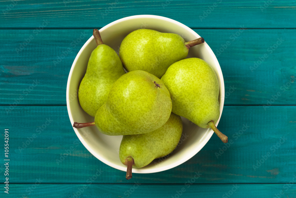 Wall mural green pears in white bowl on blue wooden background, top view.