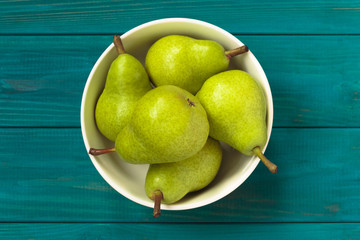 green pears in white bowl on blue wooden background, top view.