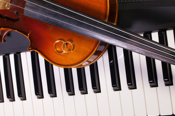 Piano keyboard, old violin and wedding rings