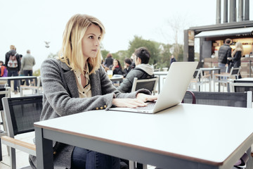 Obraz premium young beautiful female freelancer with blonde hair working in a coffee-shop outside with laptop computer