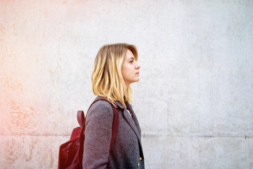 portrait of young beautiful woman with blonde hair wearing a gray coat posing on a background of gray concrete wall with copy space area for your text or design