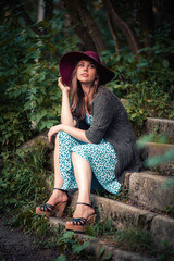 pretty slim girl with long hair in an elegant hat in a simple flowered dress in warm jacket with a...