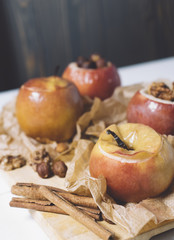Baked apples with cinnamon sticks and hazelnuts on parchment paper and cutting board on black wooden background