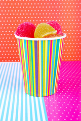 paper cup with colored lines with marmalade on a colored background. Candy in a glass on a bright background. Multi-colored sweets.