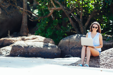 Beautiful young woman working with laptop on the tropical beach