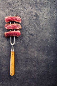 Slices of sirloin beef steak on meat fork on concrete background.