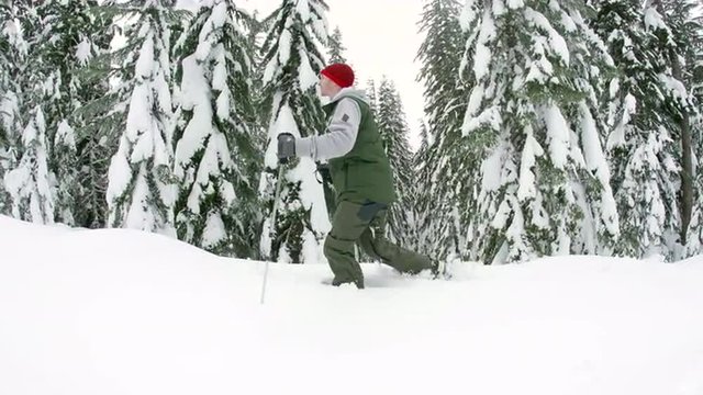 Steadicam of Man Hiking with Poles and Snowshoes Through Deep Powder by Trees