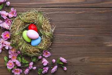 Easter eggs in nest on rustic wooden planks with flowers
