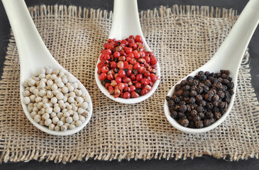 Black pepper, Piper nigrum. White pepper. Pink pepper. Different peppercorns on a rustic wooden...