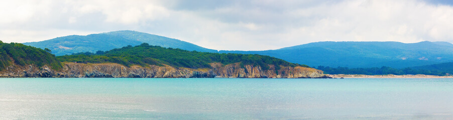Rocks, mountains and sea. Rocky shore wooded mountains and the sea. Beautiful seascape. Panoramic shot.