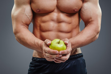 shirtless bodybuilder holding an apple in his hands.