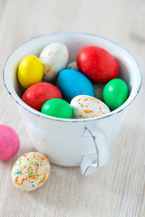 Easter candy eggs in miniature cup on wooden surface