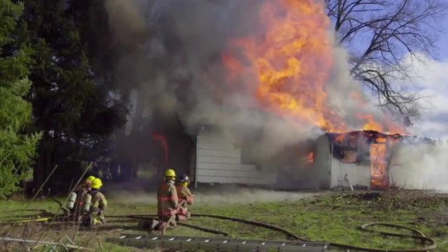 Four firemen with two hoses spray water on a burning house 