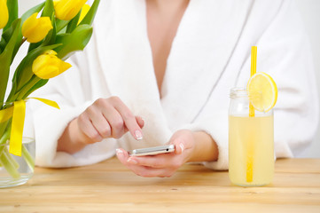 Woman in a white Bathrobe uses a smartphone. On the table yellow