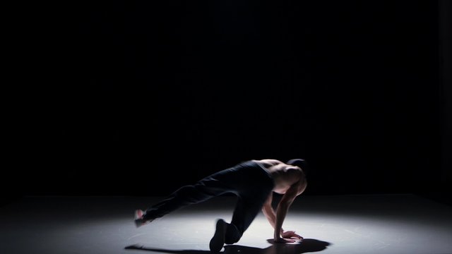 Breakdance dancer man with naked torso starts dance, on black, shadow