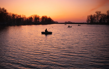 Beautiful landscape with orange sunrise, lake and fishermen 