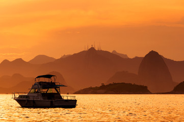 Fototapeta na wymiar Lonely Boat in the Ocean by Sunset with Rio de Janeiro Mountains in the Horizon