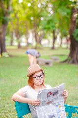 Asian female sitting on a wooden bench and reading a newspaper in a park