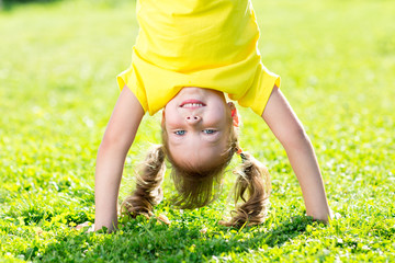 kid girl standing upside down on her head on grass in summer