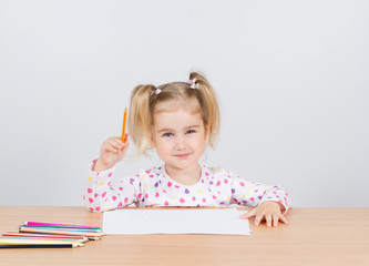 Little girl draws at table pencils.