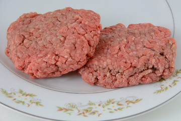 Two uncooked hamburger patties on plate in preparation of grilling or cooking