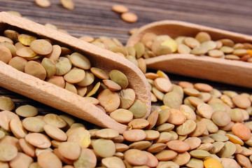 Heap of green lentil with spoon on wooden background