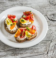 Tomato and cheese bruschetta on a white plate on rustic light wooden board. Healthy breakfast, snack or appetizer with wine