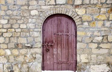 Photo of old wooden door with hinges iron in a stone wall of an old fortress