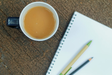 Obraz na płótnie Canvas A mug of milk tea and notepad with pen on wooden table. Selected focus. 