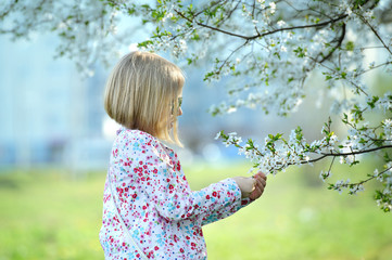 Fototapeta na wymiar Beautiful happy little girl enjoying smell in a flowering sprin