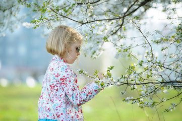 Beautiful happy little girl  enjoying smell in a flowering sprin