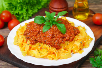 Traditional Italian pasta Bolognese or Bolognese with cooked pasta noodles topped with a spicy tomato based meat sauce garnished with fresh basil on a wooden background