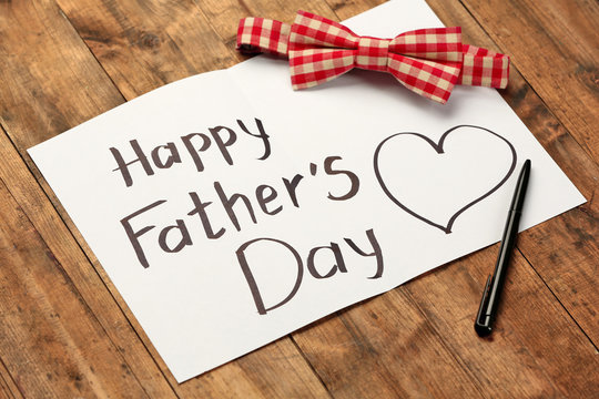 A paper sheet with Happy father's day greeting and a plaid bow on wooden background