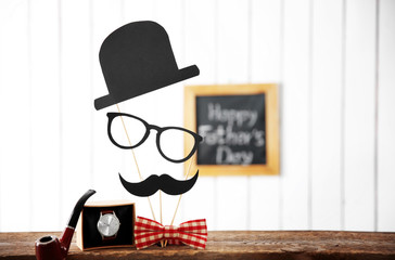 Happy Father's Day inscription at blackboard with bow tie, pipe and watch on wooden table