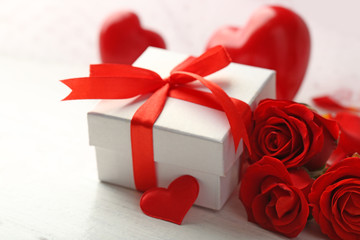 Gift box, rose flowers and decorative hearts on light wooden background