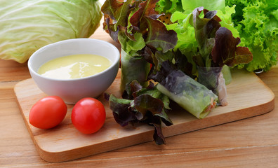 Salad roll vegetables with salad dressing in dish on wooden